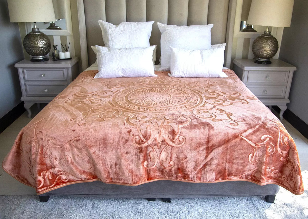 A plush, dusty rose velvet blanket with an intricate embroidered mandala and scroll pattern, styled on a bed with white pillows in a modern bedroom setting.