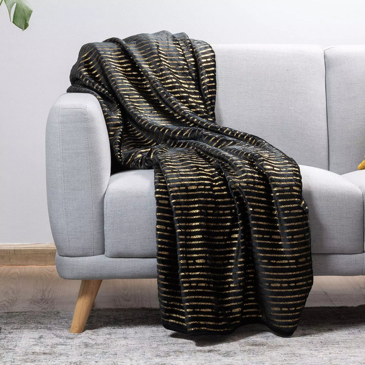 A black throw blanket with a textured gold horizontal stripe pattern draped over a light gray fabric sofa in a modern living room setting.