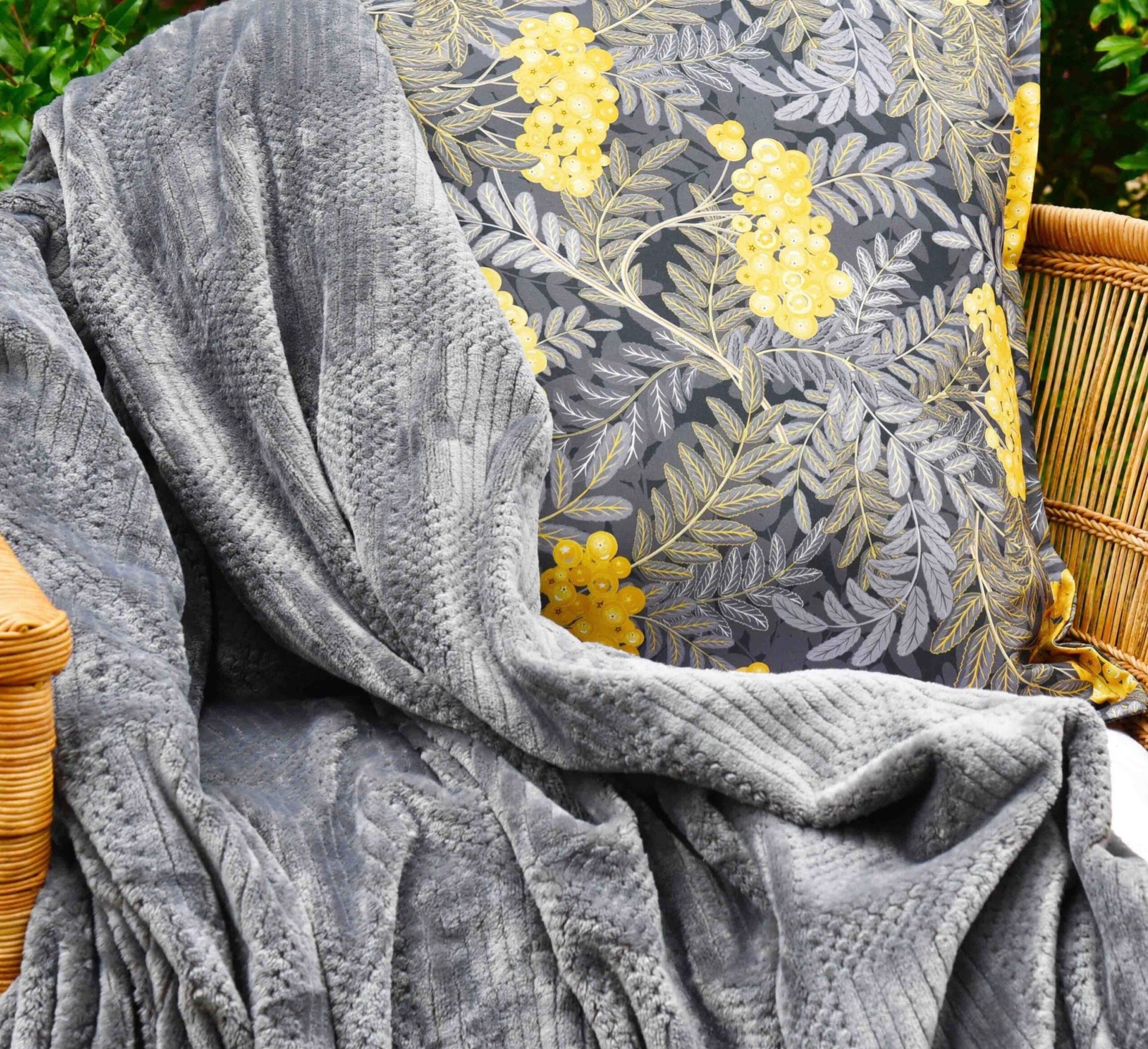 Gray textured blanket draped over a chair with a floral patterned cushion in the background.