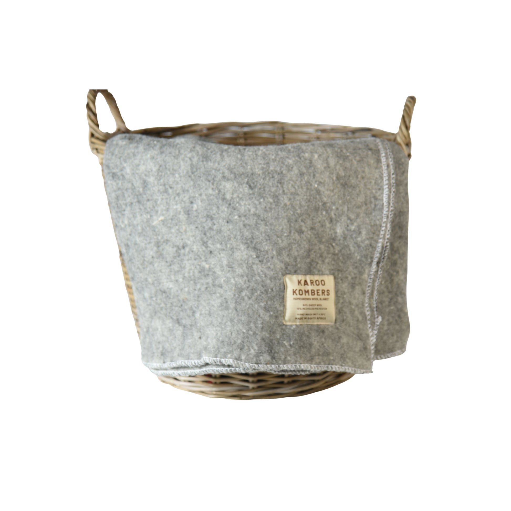A grey wool blanket in a natural wicker basket, featuring a beige brand label that reads 'KAROO KOMBERS'