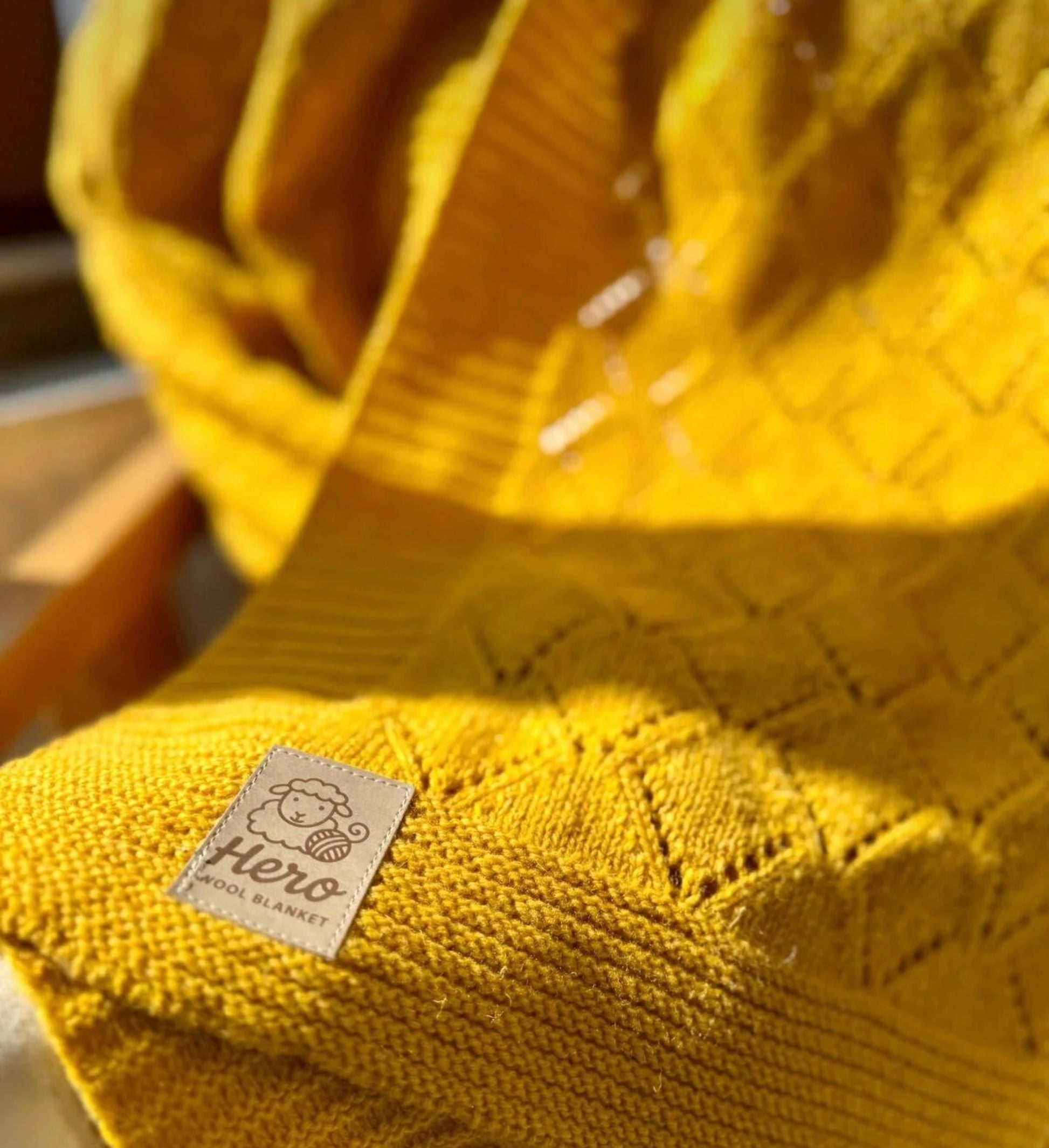 Yellow knitted blanket with a 'Hero' label on a wooden surface