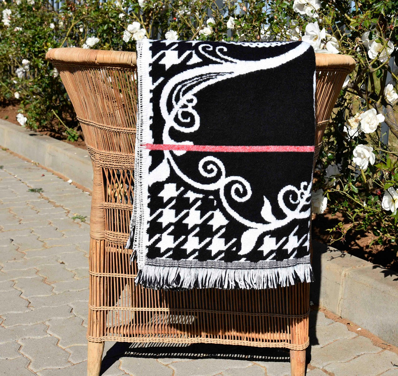 Black and white patterned Basotho blanket draped over a wicker chair with a garden background