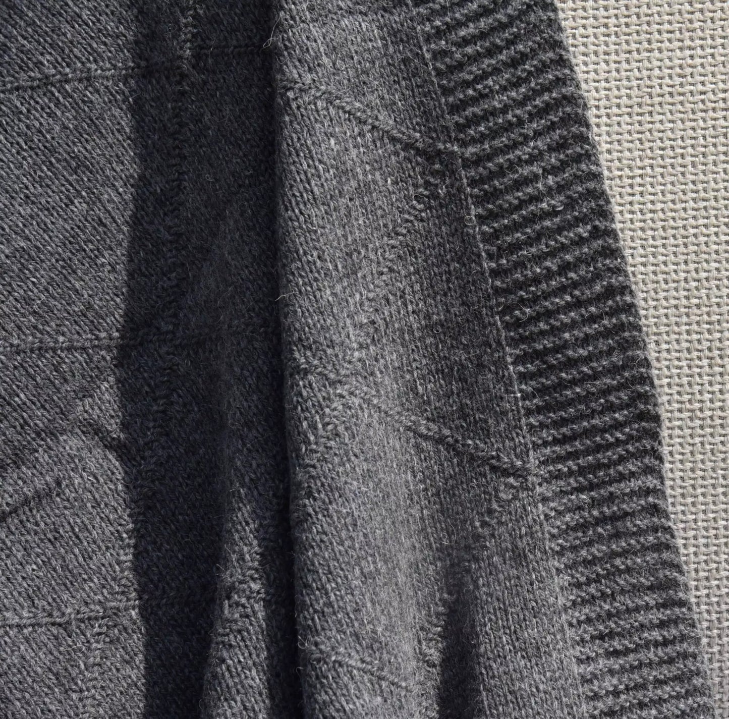 Close-up of a dark grey knitted blanket with ribbed and textured patterns, showing the material detail and stitching.