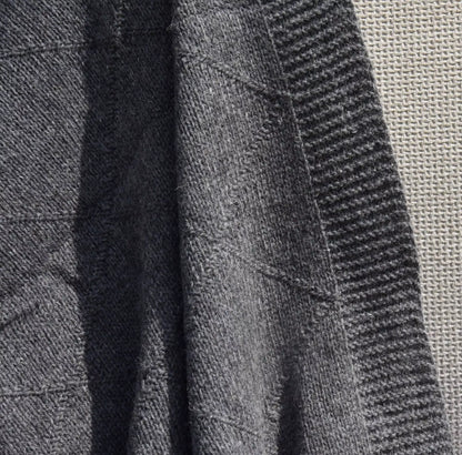 Close-up of a dark grey knitted blanket with ribbed and textured patterns, showing the material detail and stitching.
