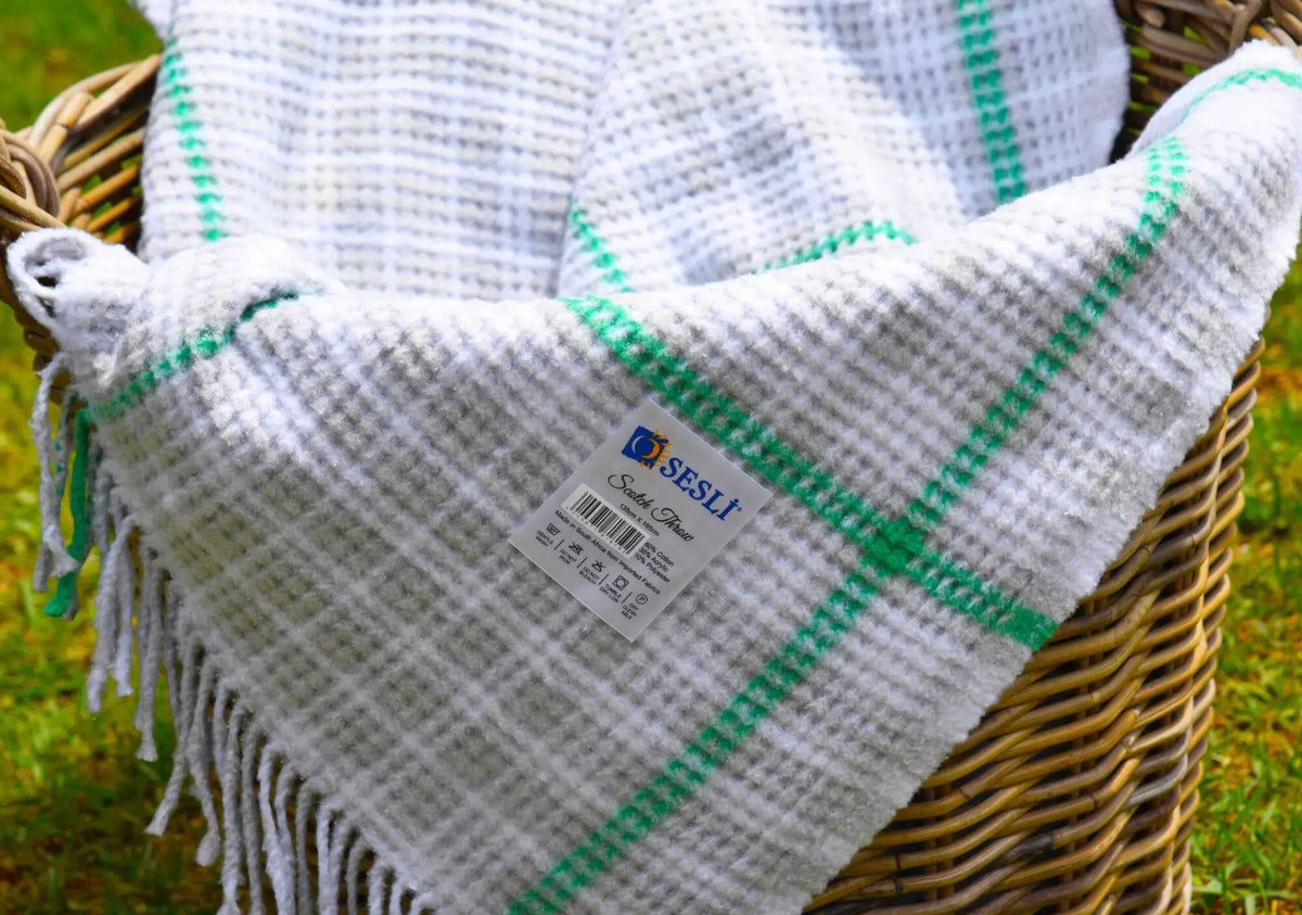White and green checkered blanket with fringes on a woven basket against a grassy background