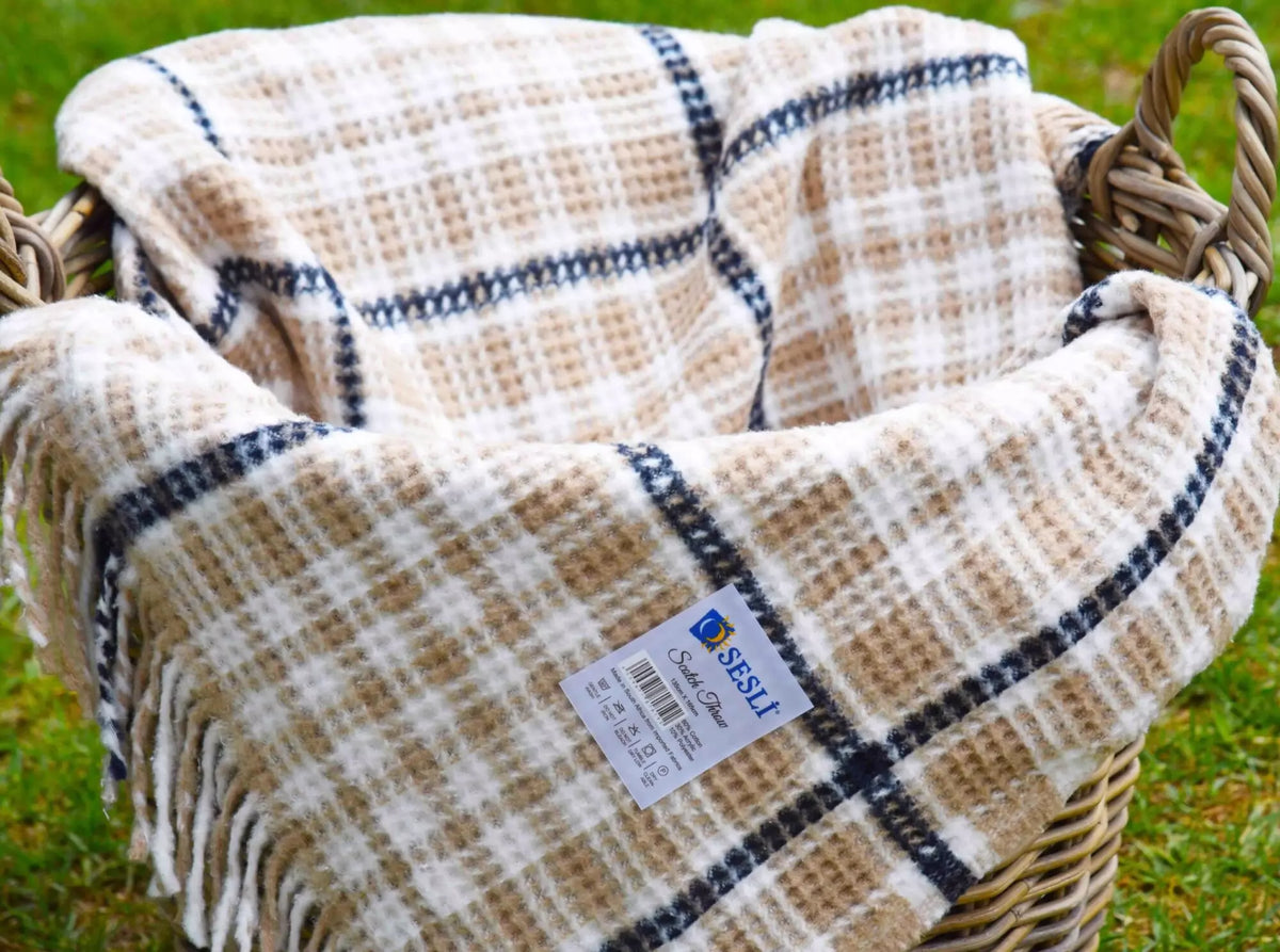 Plaid blanket with a brand label on a woven basket against a grassy background
