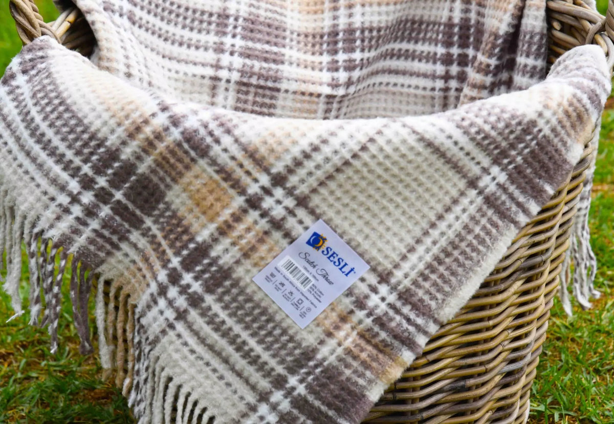 Plaid blanket with fringes draped over a wicker basket on grass