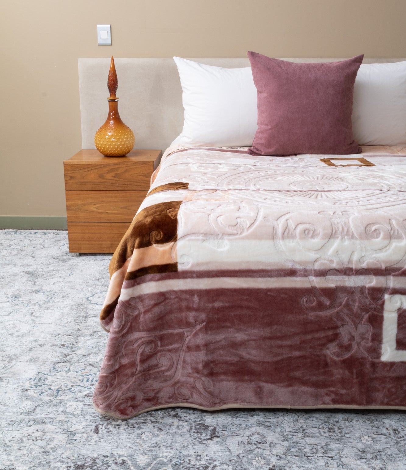 Bed with a patterned blanket with imprinted designs, decorative pillows, and a nightstand in a bedroom setting.