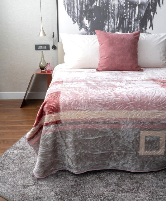 Bed with pink and grey blanket that has imprinted designs and pillow in a bedroom setting.