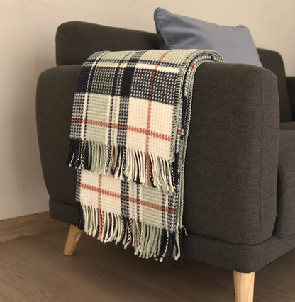 A woven plaid throw blanket with fringe, draped over the arm of a dark gray armchair in a living room setting.