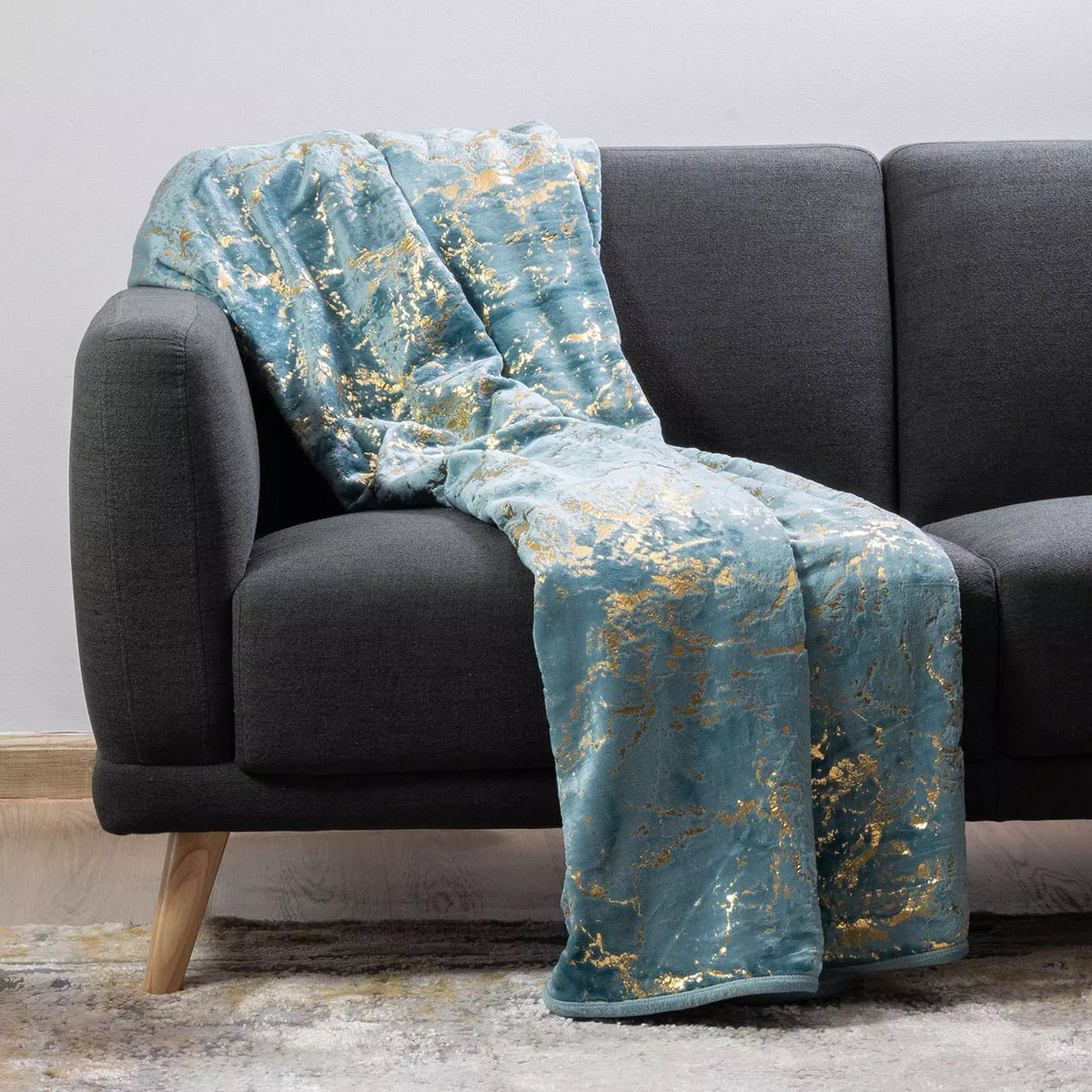 A teal blue throw blanket with a gold marble pattern draped over a dark gray fabric sofa.