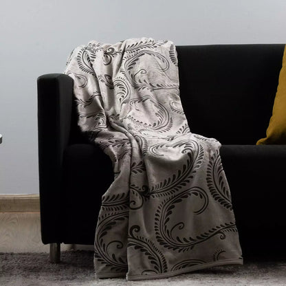 A beige and black  throw blanket with a black ornate scroll pattern draped over a black sofa in a living room setting.