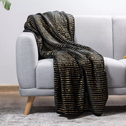 A black throw blanket with a textured gold horizontal stripe pattern draped over a light gray fabric sofa in a modern living room setting.