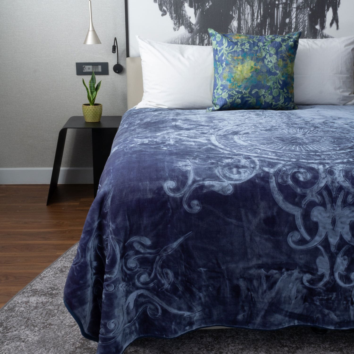 Bedroom with a bed featuring a blue blanket that has imprinted designs and a decorative pillow.