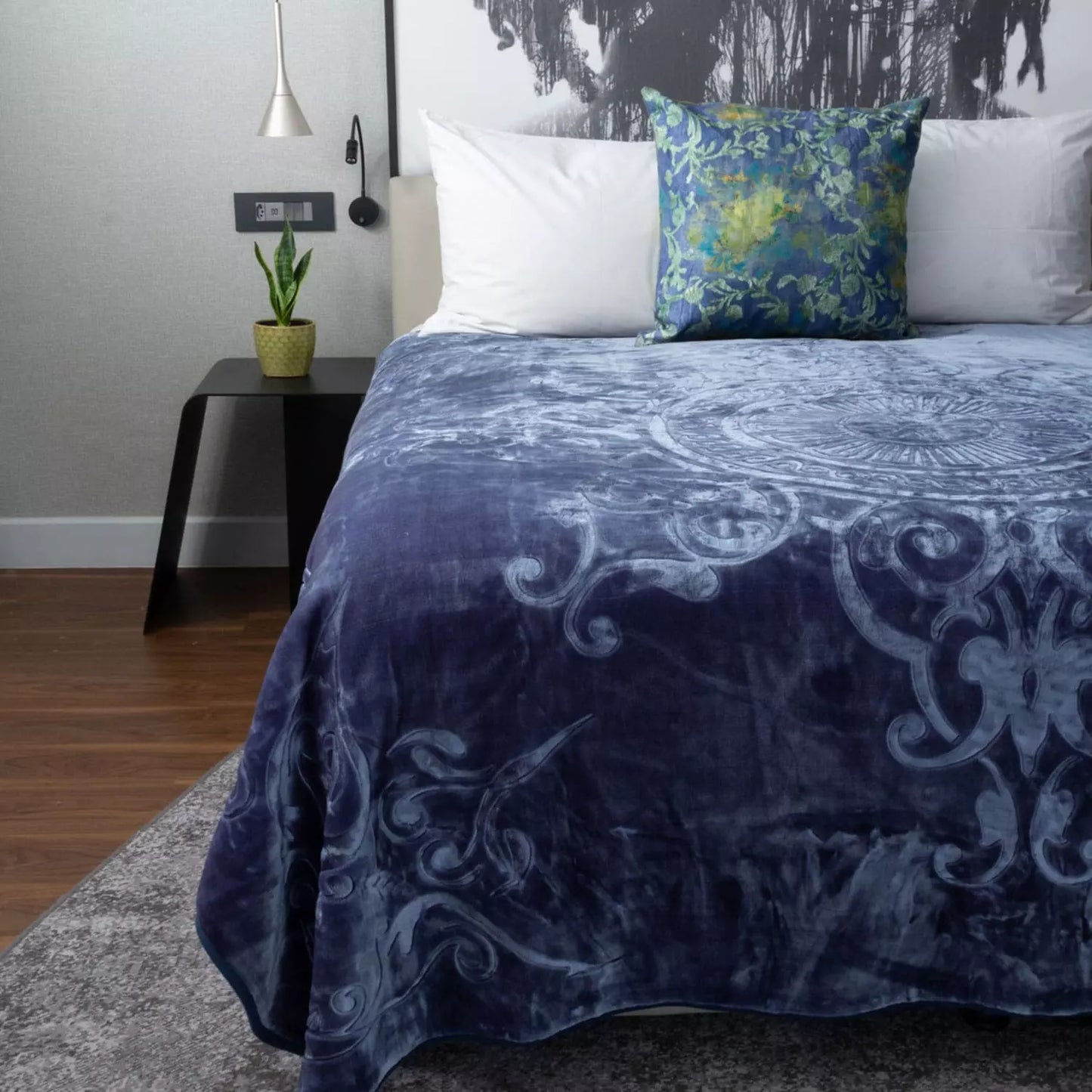 Bed with blue patterned blanket and floral pillow in a bedroom setting.