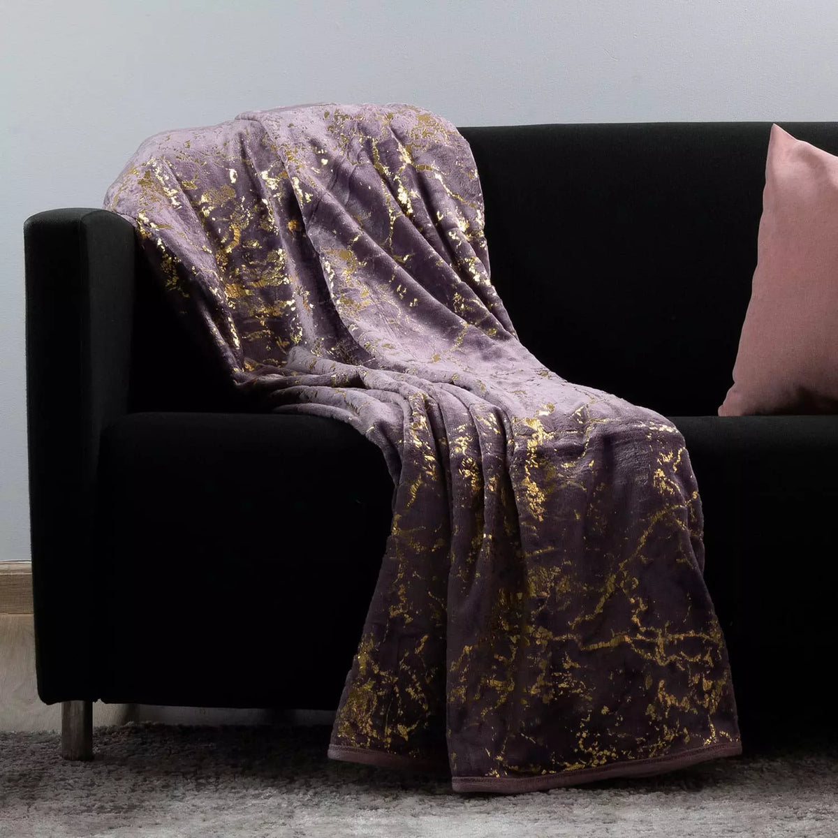 Purple textured blanket draped over a black armchair with a pink pillow.