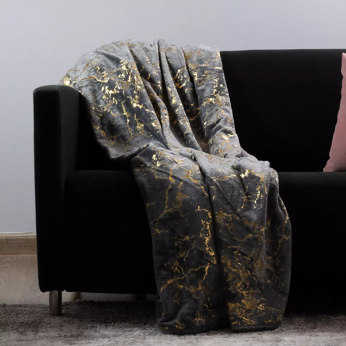 A plush throw blanket with a black and gold marble pattern draped over a black sofa in a living room setting.