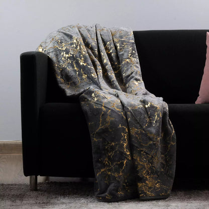 A plush throw blanket with a black and gold marble pattern draped over a black sofa in a living room setting.