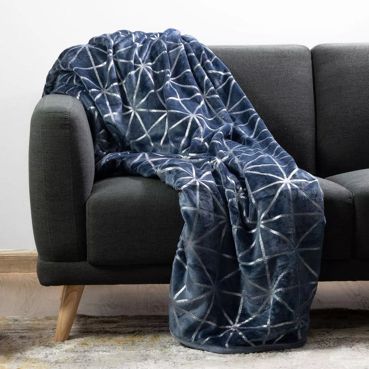 An indigo throw blanket with a silver geometric starburst pattern draped over a dark grey fabric sofa.