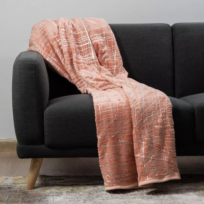 A peach-pink fleece throw blanket with a white grid pattern draped over a dark gray fabric sofa.